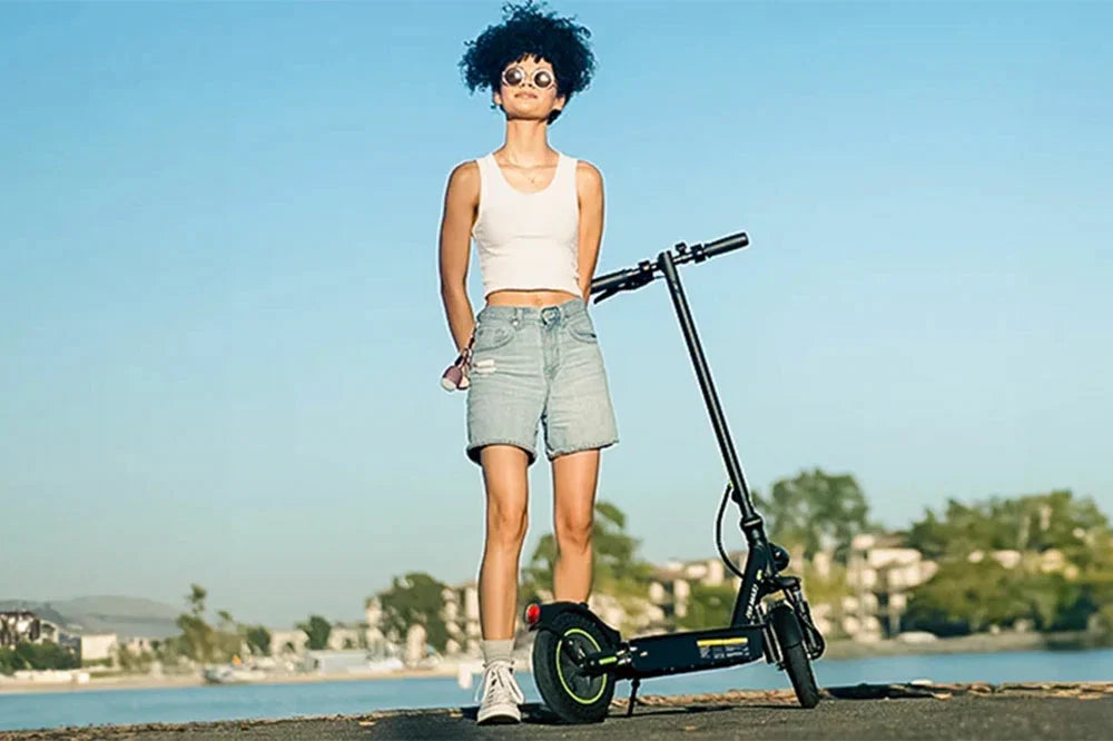 Woman standing beside foldable electric scooter at seaside, urban commuter e‑scooter